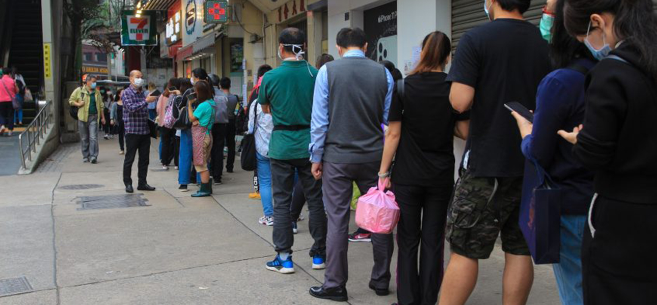 People in masks wait in line on a street