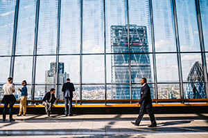 Man walks past window of a skyscraper overlooking a cityscape.