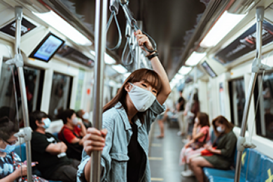 Woman in mask looks at camera while standing and holding a pole on a train