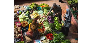 Woman sells fresh fruit and vegetables to a couple at a market stall