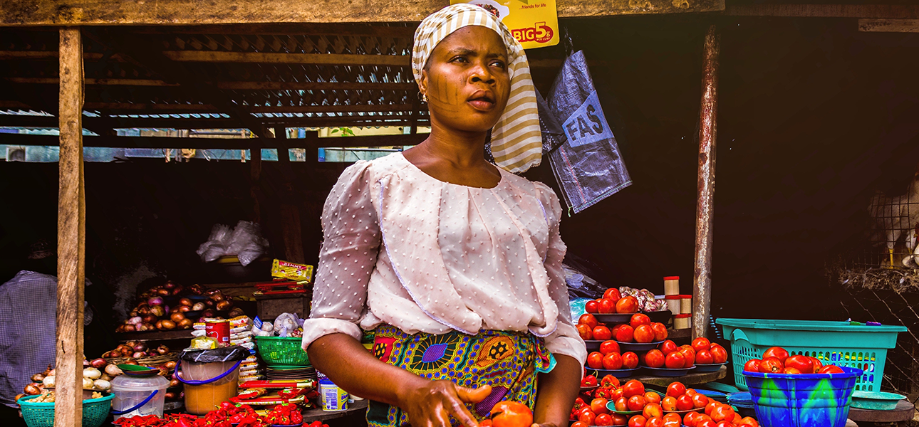 Woman holds tomatoes for sale at an open air market, looking up into the distance.